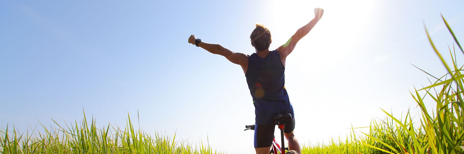 Young rider with bicycle standing in a green lush meadow with raised hands